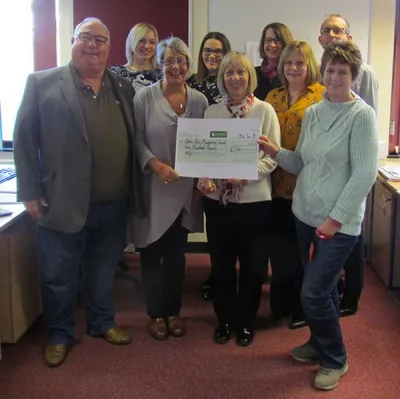 Martin and Dianne Parr (front row, left and second from left) receive the £500 cheque from members of Leek United’s Mortgage Operations team.